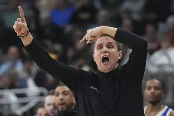 مدرب فريق ماكنيس ويل ويد يوجه لاعبيه بحماس خلال مباراة NCAA، مع تفاعل الجمهور في الخلفية.
