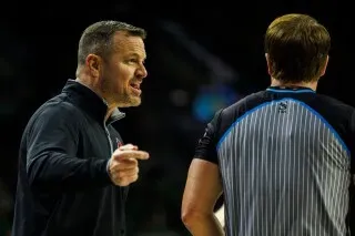 مدرب يتحدث بحماس مع حكم خلال مباراة كرة سلة، مع التركيز على تعبيراته الجادة، مما يعكس التوتر في المنافسة.