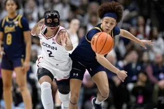 لاعبة كرة سلة تتنافس على الكرة خلال مباراة، مع التركيز على الحركة السريعة والتوتر بين اللاعبين.