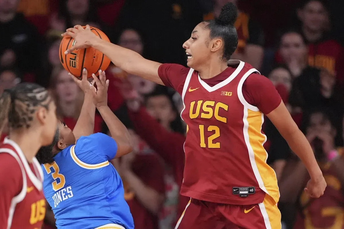 لاعبة من فريق USC (رقم 12) تعترض تسديدة لاعبة UCLA (رقم 3) خلال مباراة كرة السلة، مع جمهور متحمس في الخلفية.