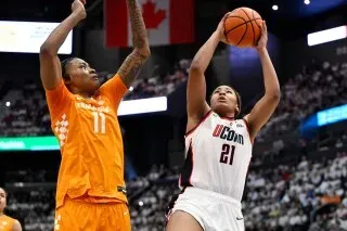 لاعبة كرة سلة من فريق يوكون تسجل نقطة خلال مباراة ضد فريق تينيسي، مع وجود لاعب منافس يحاول الدفاع عنها.