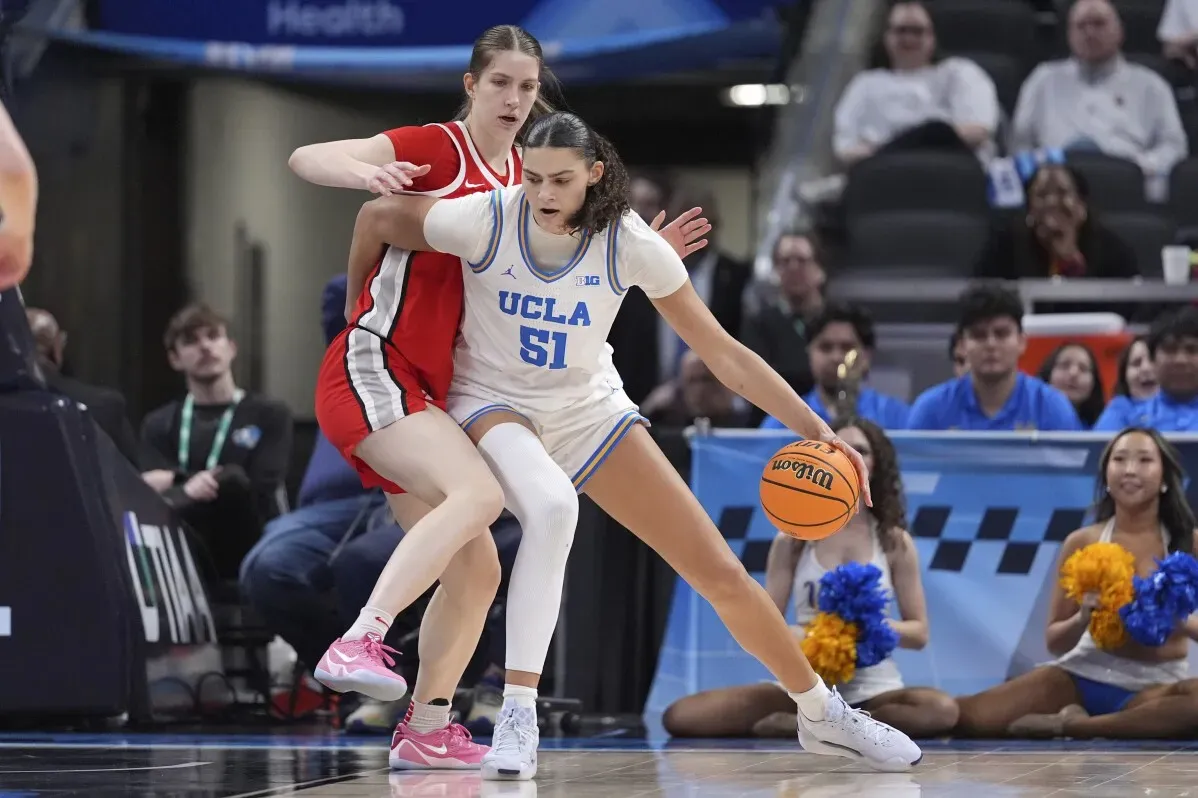 لاعبة UCLA تتنافس مع لاعبة من فريق آخر في مباراة كرة سلة جامعية، مع التركيز على الكرة والتكتيك الرياضي.