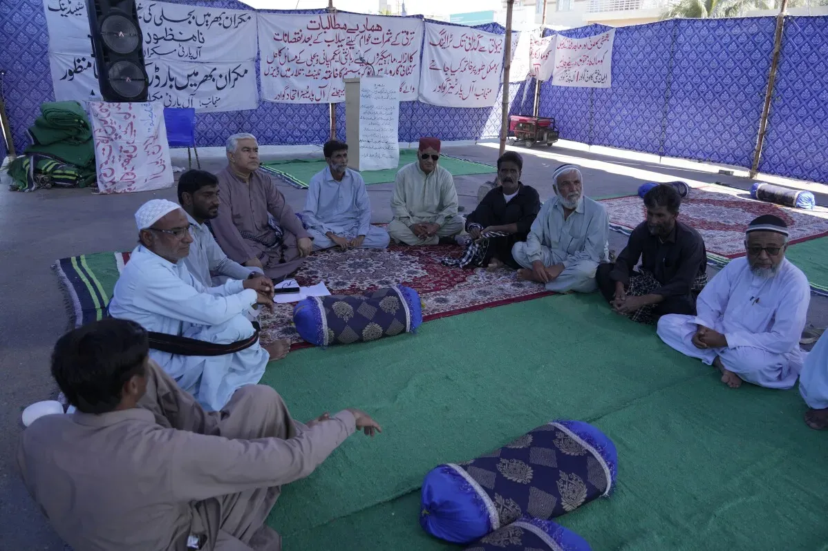 مجموعة من الرجال يجلسون في حلقة نقاش في جوادر، باكستان، مع لافتات خلفهم تعبر عن مطالبهم واحتياجاتهم.