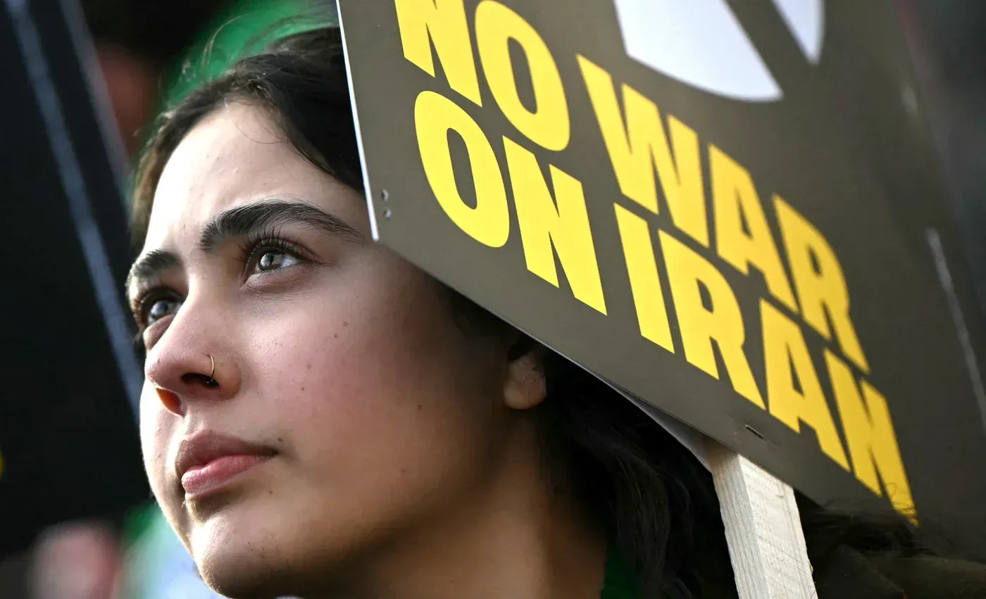 امرأة تحمل لافتة مكتوب عليها "لا للحرب على إيران" تعبر عن موقفها ضد النزاع العسكري، معبرة عن مشاعر القلق والتضامن.