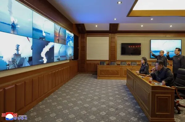 كيم جونغ أون وابنته يشاهدان إطلاق صواريخ كروز استراتيجية عبر شاشة في غرفة اجتماعات، مع التركيز على العمليات العسكرية لكوريا الشمالية.