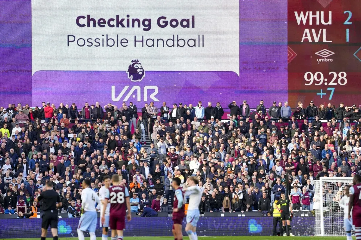 حشود الجماهير في ملعب كرة القدم أثناء مشاهدة شاشة تبين مراجعة تقنية حكم الفيديو المساعد (VAR) لقرار يتعلق باللمس المحتمل.