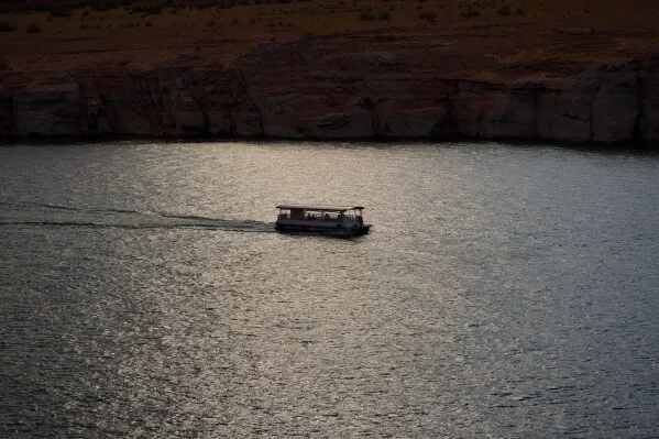 قارب صغير يبحر على مياه نهر Colorado قرب سد Glen Canyon في أريزونا وسط انخفاض منسوب المياه وتأثيرات تغير المناخ على توليد الكهرباء والحياة البرية.