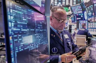 تاجر في بورصة الأسهم الأمريكية يتفاعل مع شاشات تعرض بيانات الأسواق، وسط تراجع مؤشرات الأسهم وتأثير أسعار النفط.