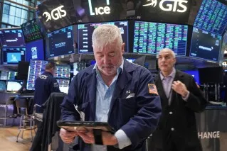 متداول في بورصة وول ستريت يستخدم جهاز لوحي لمتابعة حركة الأسهم، مع شاشات تعرض أسعار الأسهم في الخلفية.