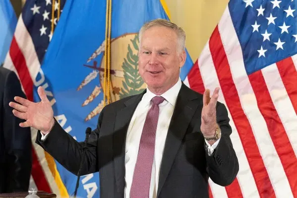 آلان أرمسترونغ يتحدث في مؤتمر صحفي بعد تعيينه في مجلس الشيوخ الأمريكي، مع أعلام أوكلاهوما والولايات المتحدة خلفه.