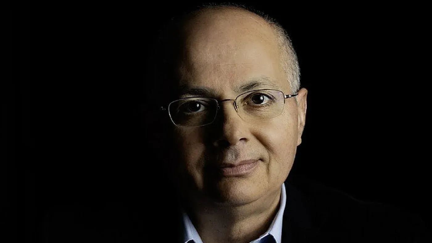 عالم الكيمياء عمر ياغي، الحائز على جائزة نوبل، يظهر في صورة مع خلفية داكنة، معبرًا عن إنجازاته في الهندسة الجزيئية.