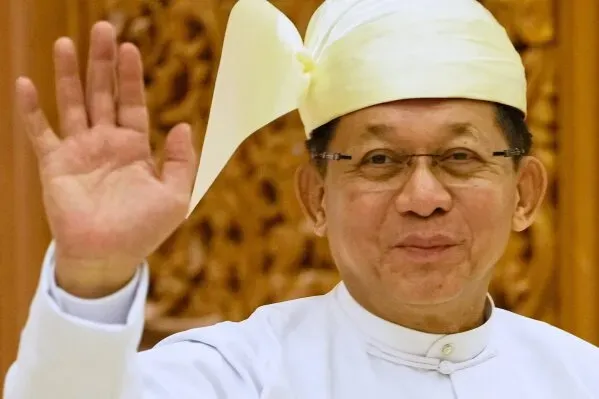 صورة لرجل يرتدي زيًا تقليديًا بورميًا، مبتسمًا ويُلوّح بيده، يعكس الأجواء السياسية المتوترة في ميانمار.