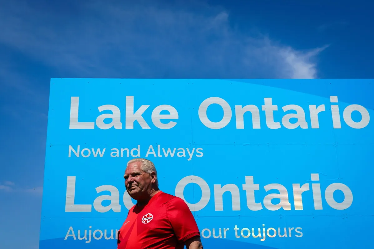 دوغ فورد رئيس حكومة أونتاريو يقف أمام لافتة ضخمة مكتوب عليها "Lake Ontario الآن وإلى الأبد" ردًا على محاولة ترامب إعادة تسمية البحيرة.