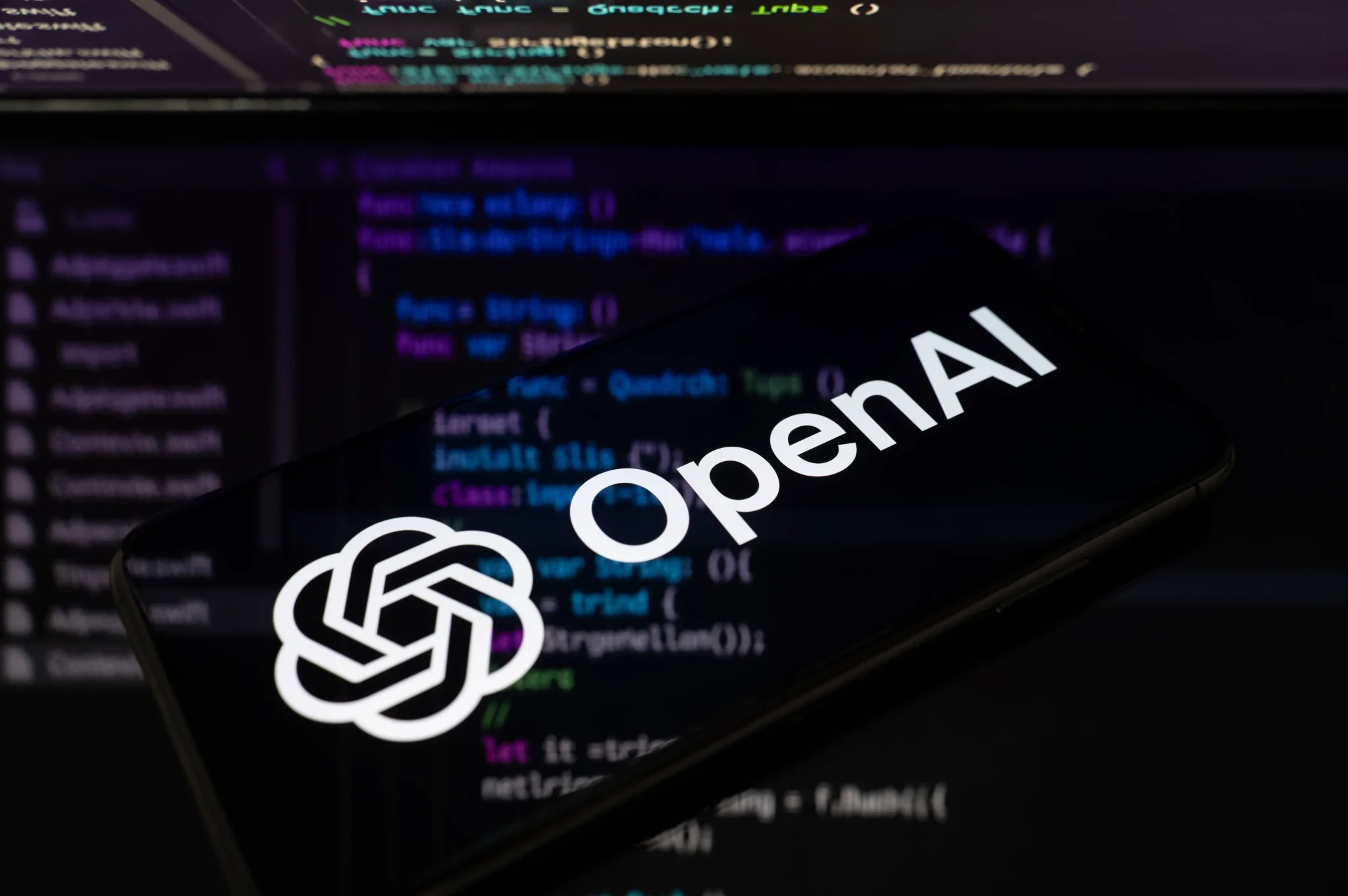 شعار OpenAI على شاشة هاتف ذكي مع خلفية شفرة برمجية، يعكس نقاش سلامة الذكاء الاصطناعي وثقافة الشركات التقنية.