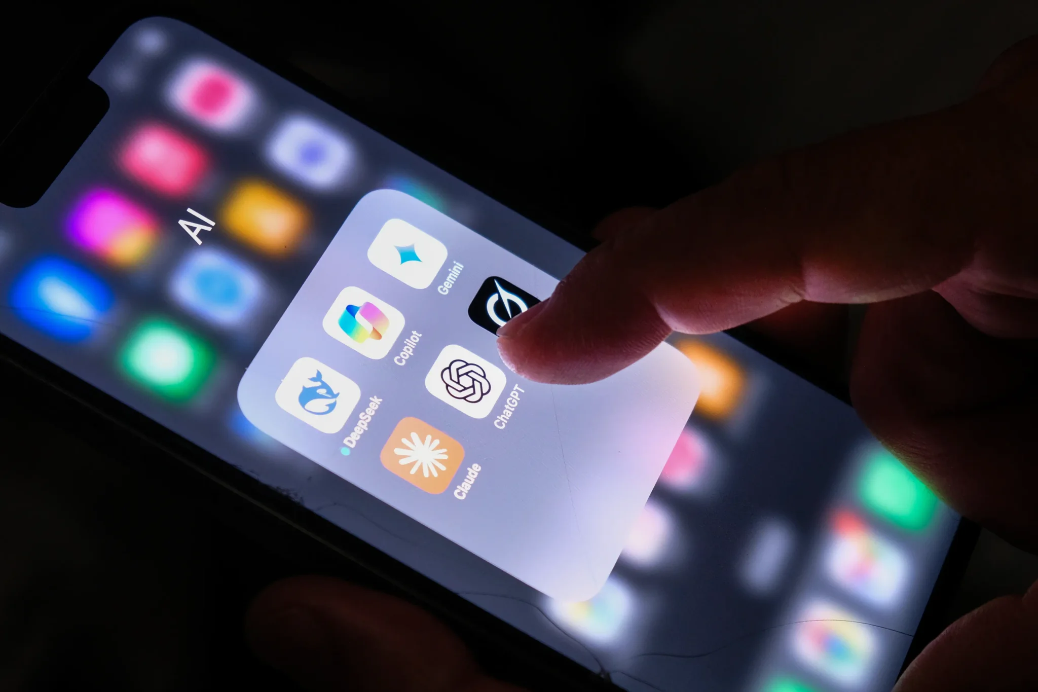 شاشة هاتف تعرض مجلد تطبيقات ذكاء اصطناعي مع تمييز تطبيق ChatGPT، مع إشارة إصبع تلمس الشاشة في سياق أدوات العمل التعاوني والذكاء الاصطناعي.