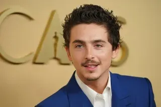 مرشح لجائزة الأوسكار يرتدي بدلة زرقاء، مبتسمًا أمام خلفية تحمل شعار الأوسكار، خلال مأدبة الغداء للمرشحين في بيفرلي هيلز.