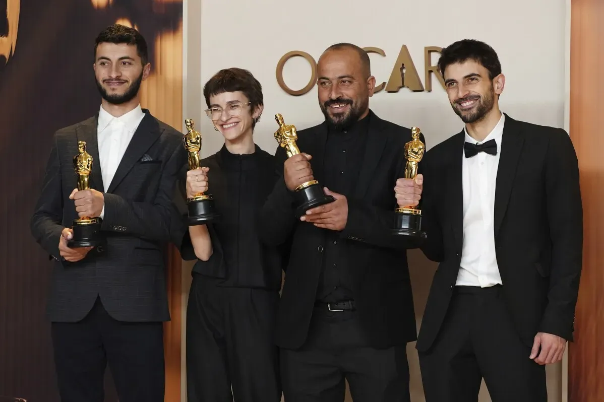 فائزون بجوائز الأوسكار يقفون مع تماثيلهم في احتفال بيفرلي هيلز، مع تعبيرات الفخر والفرح على وجوههم.