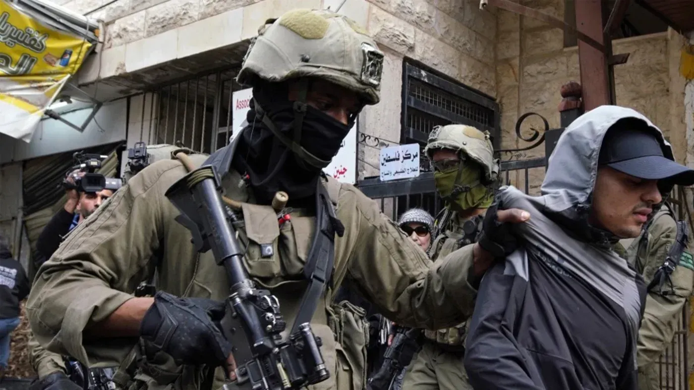جنود إسرائيليون يرتدون زيًا عسكريًا ويعتقلون شابًا في أحد شوارع فلسطين، مما يعكس التوترات المستمرة في المنطقة.