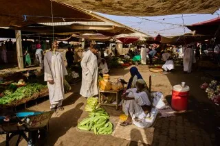 سوق مزدحم في السودان حيث يبيع الباعة الخضروات والفواكه، يعكس التحديات الاقتصادية وسط أزمة غذائية حادة.