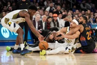 لاعبو إنديانا بيسرز يتنافسون على الكرة في مباراة مثيرة ضد نيويورك نيكس، مع وجود جمهور في الخلفية.