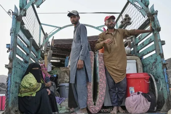 لاجئون أفغان يجلسون في شاحنة محملة بالأمتعة، مع مشهد يعكس معاناتهم أثناء الاستعداد للعودة إلى أفغانستان.