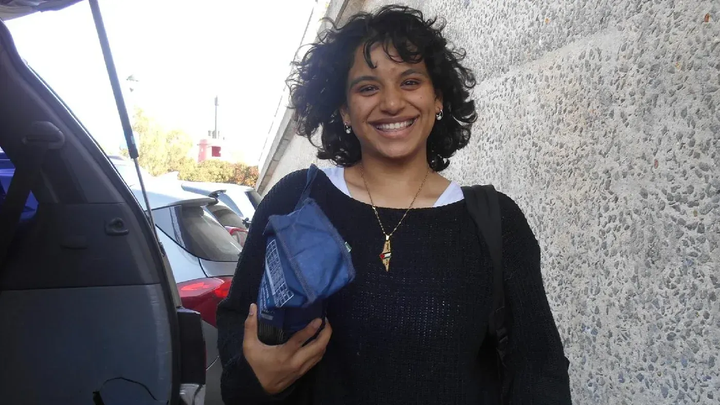 قيسر زهرة، ناشطة فلسطينية، تبتسم بينما تحمل حقيبة، في خلفية تظهر سيارات، بعد الإفراج عنها من الحبس الاحتياطي.