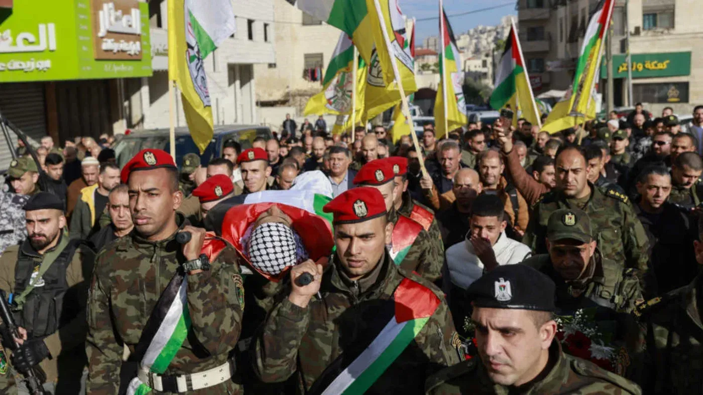 تجمع حشود من أفراد قوات الأمن الفلسطينية في جنين، يحملون نعشًا مغطىً بالعلم الفلسطيني، وسط أجواء من التوتر والمخاوف السياسية.