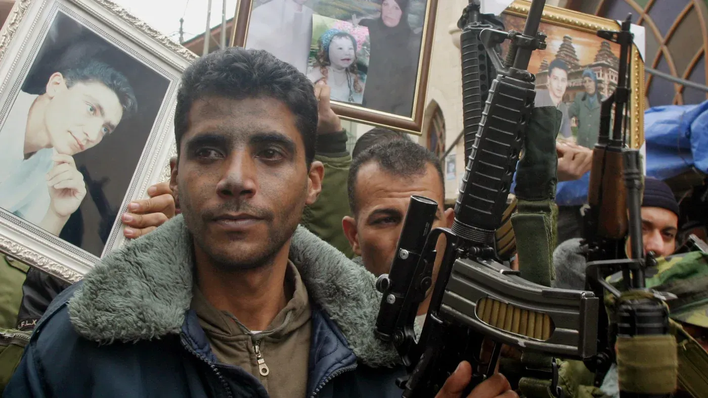 شخص يحمل سلاحًا ويظهر خلفه آخرون يحملون صورًا لأسرى فلسطينيين، في إطار تأكيد الدعم للقضية الفلسطينية.