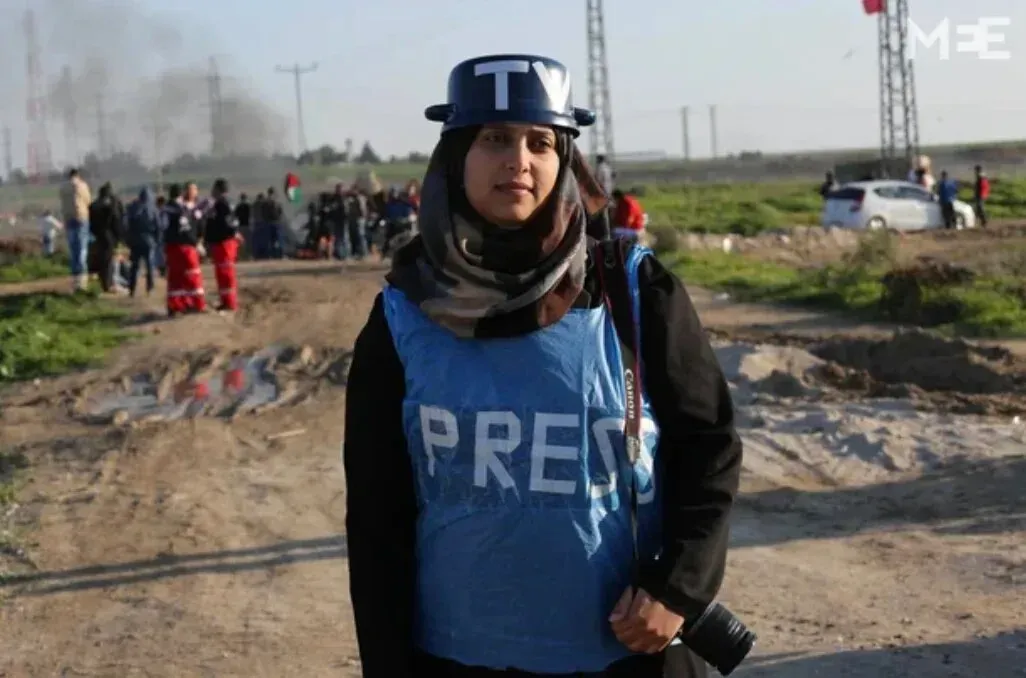 سمر أبو العوف، مصورة فلسطينية ترتدي سترة "PRESS" وخوذة، تقف في موقع تصوير في غزة، تعكس التحديات التي تواجه الصحفيين في المنطقة.