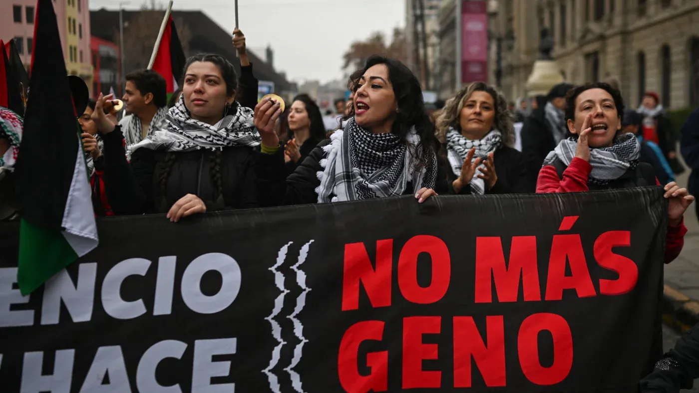 نساء يحملن لافتة خلال مظاهرة في تشيلي تطالب بوقف الإبادة في غزة، مع تواجد أعلام فلسطينية وشعارات تدعو إلى العدالة.