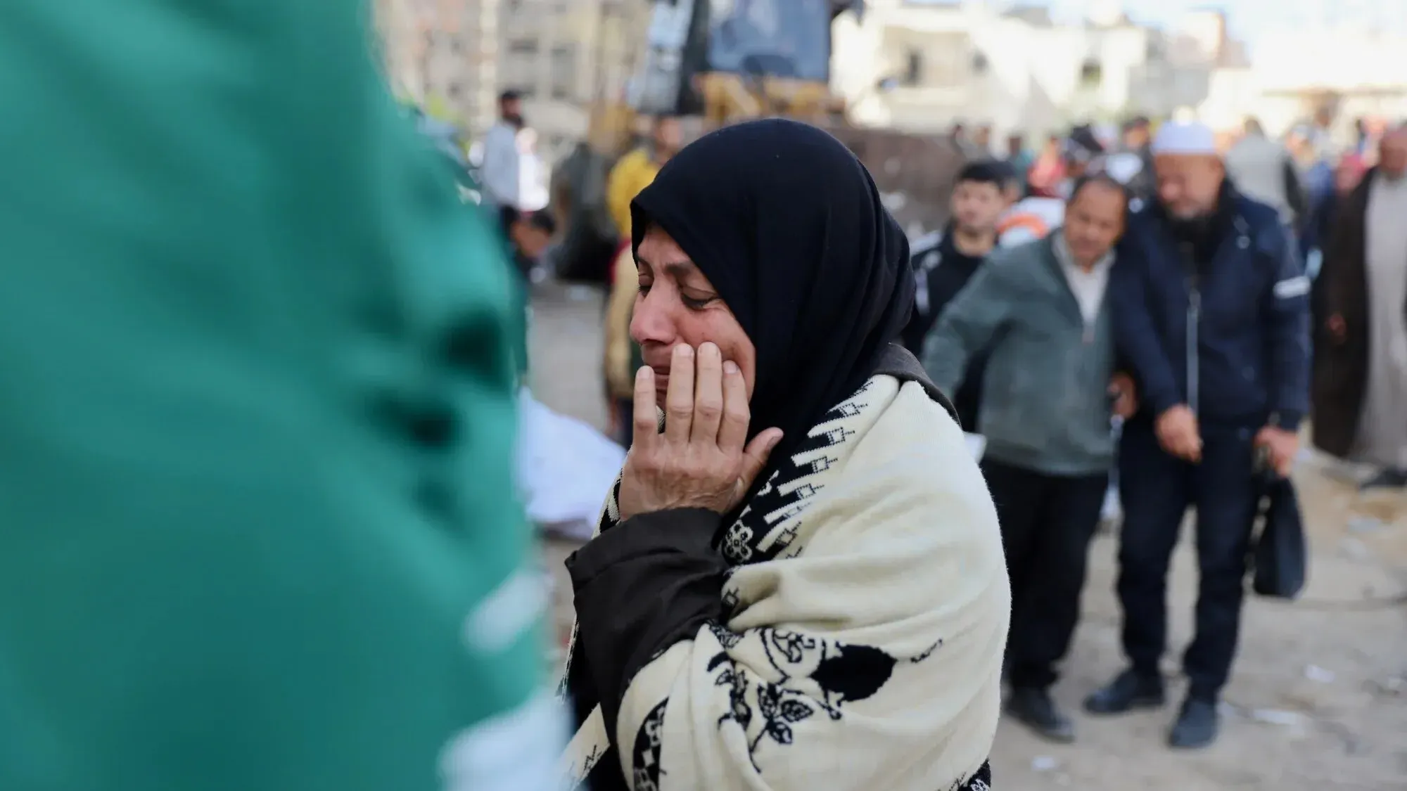 امرأة فلسطينية تبكي أثناء البحث عن رفات ابنها في مستشفى الشفاء بغزة، محاطة بعائلات أخرى في حالة حزن عميق.