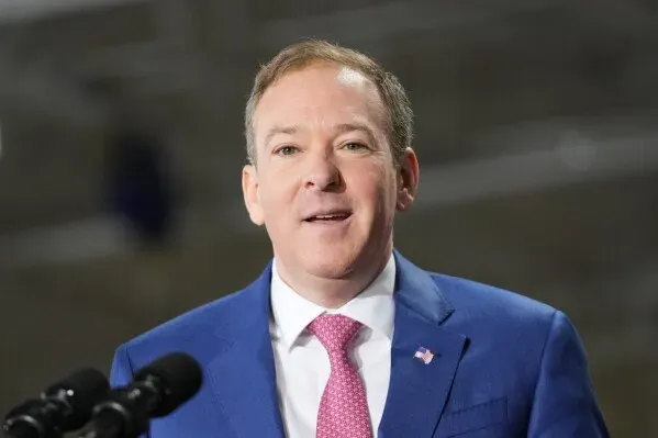 صورة لرجل يرتدي بدلة زرقاء وقميص أبيض وربطة عنق وردية، مبتسمًا أثناء إلقاء كلمة. تعكس الصورة أجواء سياسية في سياق مغادرة بام بوندي لوزارة العدل.