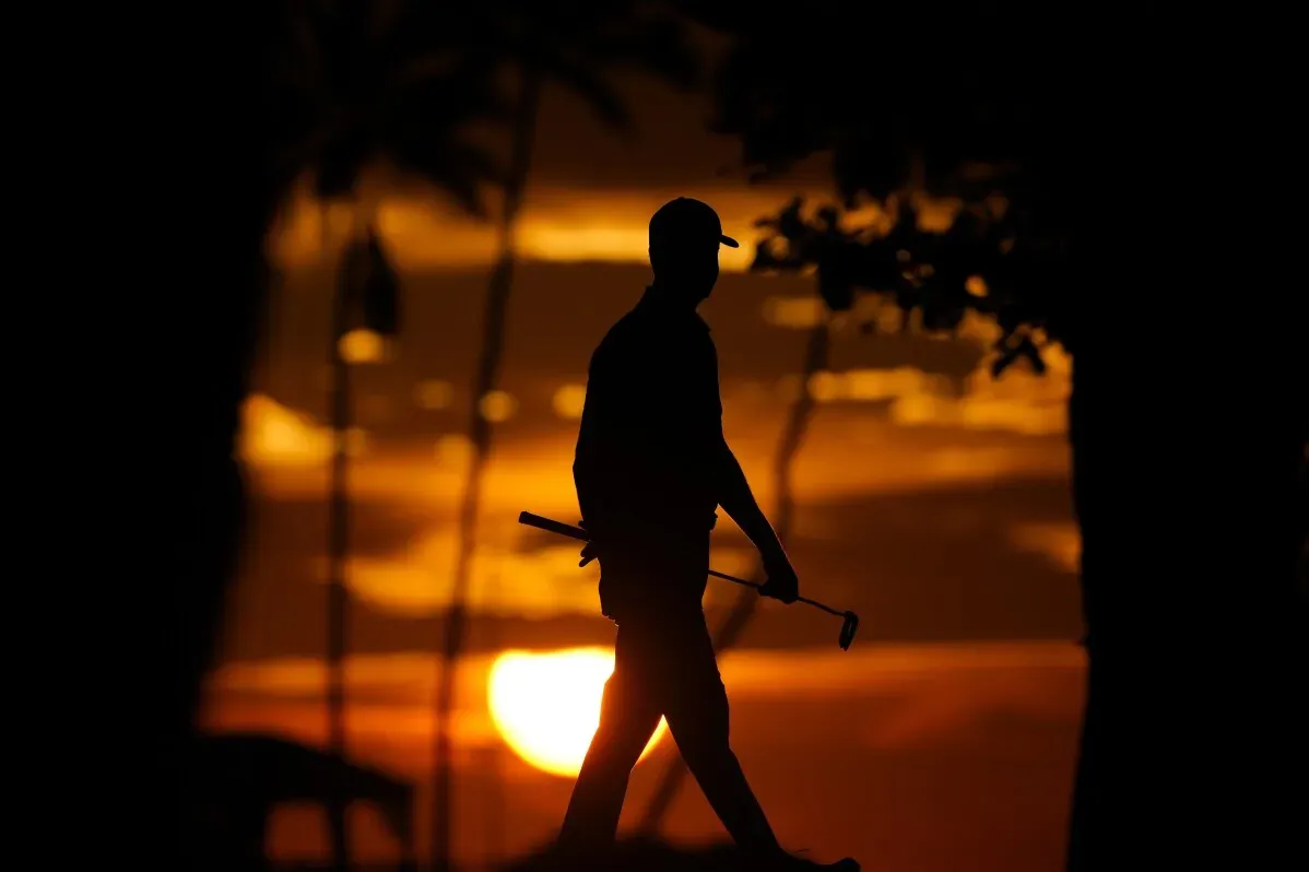 لاعب جولف يسير بخطوات هادئة مع مضرب في يده، silhouetted أمام غروب الشمس الجميل في وايالاي، هاواي.