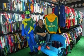 صاحب متجر "ألامبرادو فوتبول إي كولتورا" يجلس أمام مجموعة كبيرة من قمصان كرة القدم التاريخية، مع سترة بيليه الشهيرة خلفه.