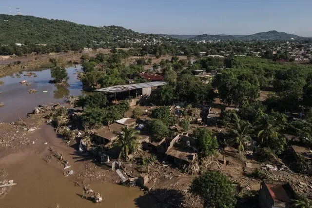 تظهر الصورة مشهدًا من بلدة ألامو في المكسيك بعد الفيضانات، حيث تضررت المنازل والأراضي بسبب الأمطار الغزيرة، مع وجود نهر يمر عبر المنطقة.