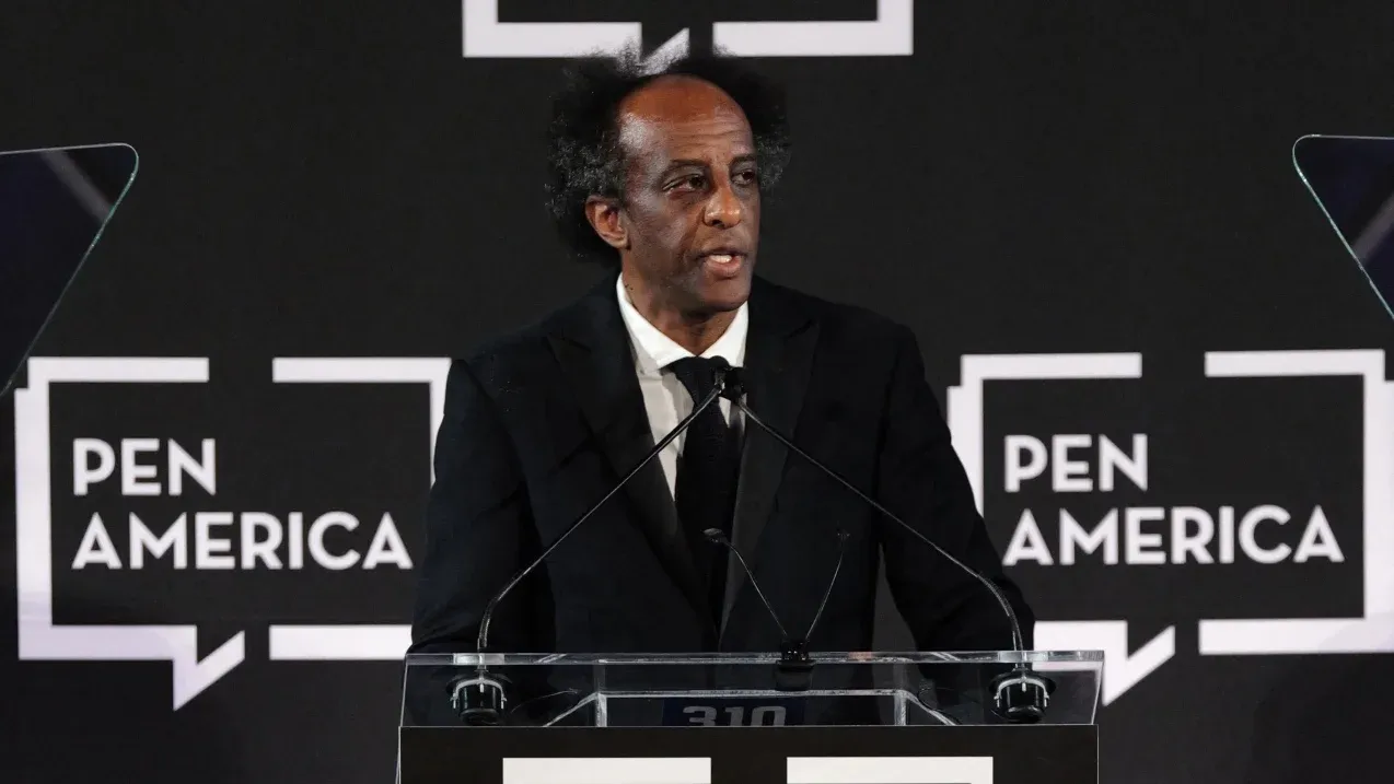ديناو منغستو يتحدث في مؤتمر Pen America، مع خلفية شعار المنظمة، بعد استقالته احتجاجًا على موقف المنظمة من حرية التعبير والمقاطعة الثقافية الفلسطينية.
