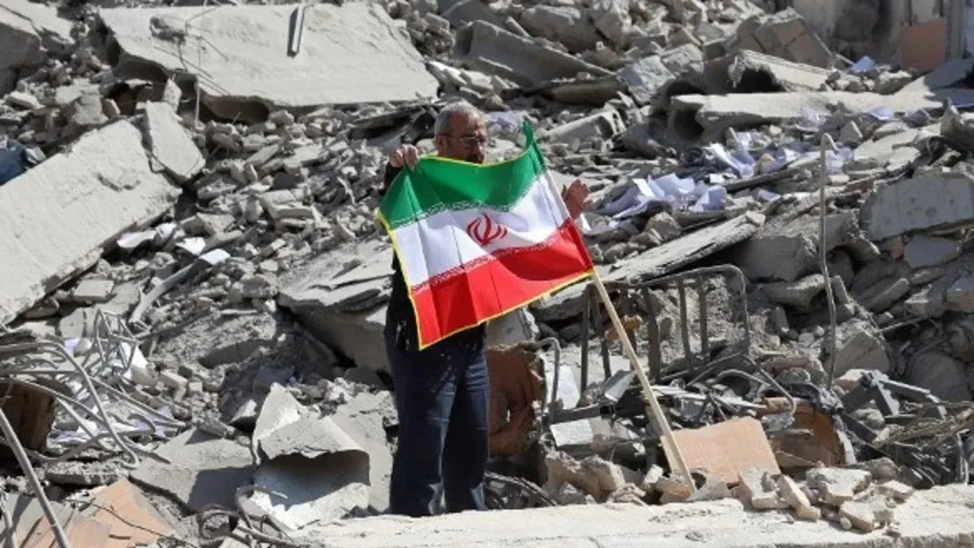 رجل يحمل علم إيران وسط أنقاض مبنى مدمر، مما يعكس آثار الصراع المستمر وتأثيره على المدنيين.