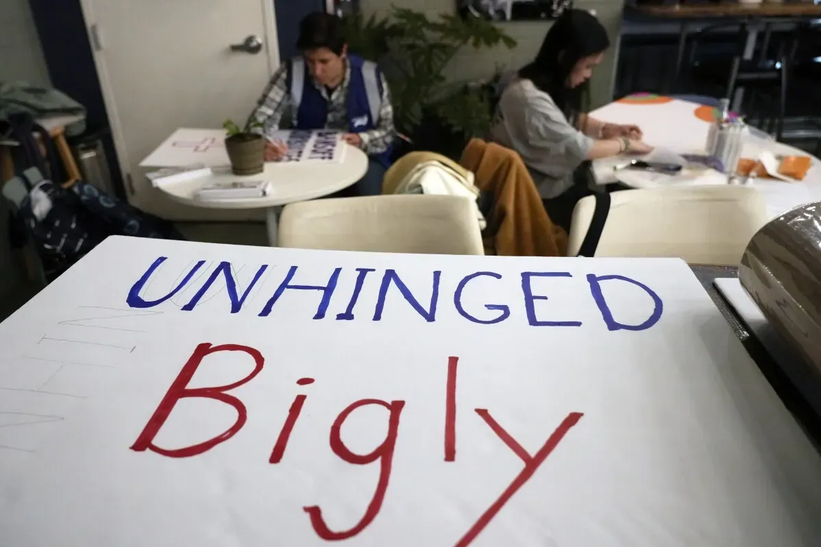 شعار كبير مكتوب عليه "UNHINGED Bigly" في ورشة عمل تحضيرية لمظاهرة النساء، مع مشاركتين في الخلفية تعملان على لافتات.