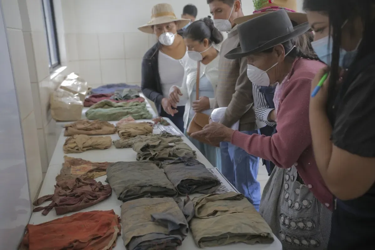 جموع من الأشخاص ينظرون إلى أقمشة ملونة مرتبة على طاولة في غرفة، يمثلون عائلات بحثت عن معلومات عن مفقوديهم في بيرو.