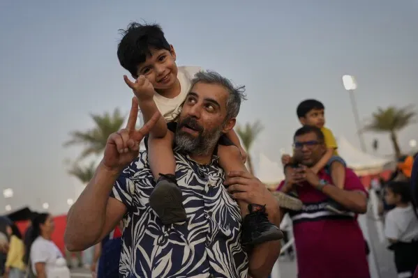رجل يحمل طفلاً على كتفيه، مع ابتسامة على وجههما، وسط أجواء سباق جائزة البحرين الكبرى، حيث يتواجد الحضور في أجواء احتفالية.