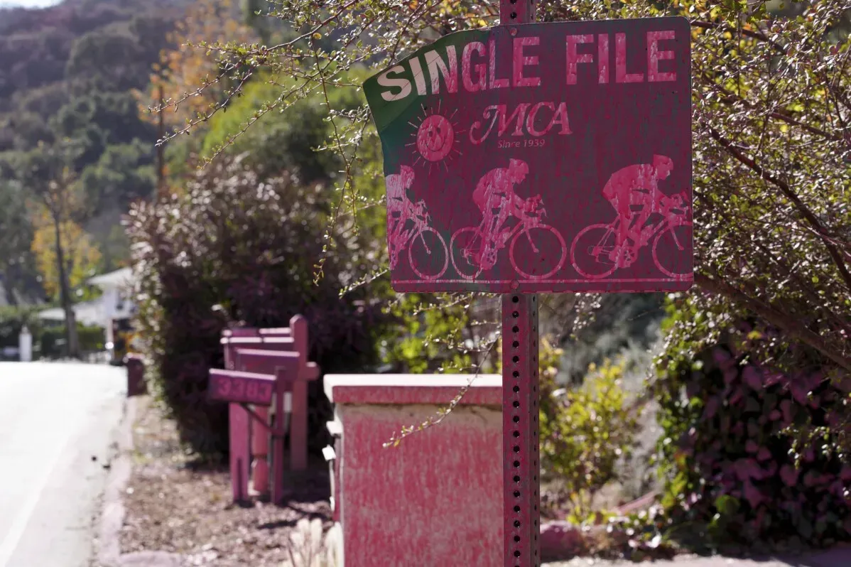 لافتة مرورية وردية اللون تحمل عبارة \"Single File\" مع رسومات لدراجين، محاطة بالنباتات والأشجار، تشير إلى منطقة مخصصة لركوب الدراجات.