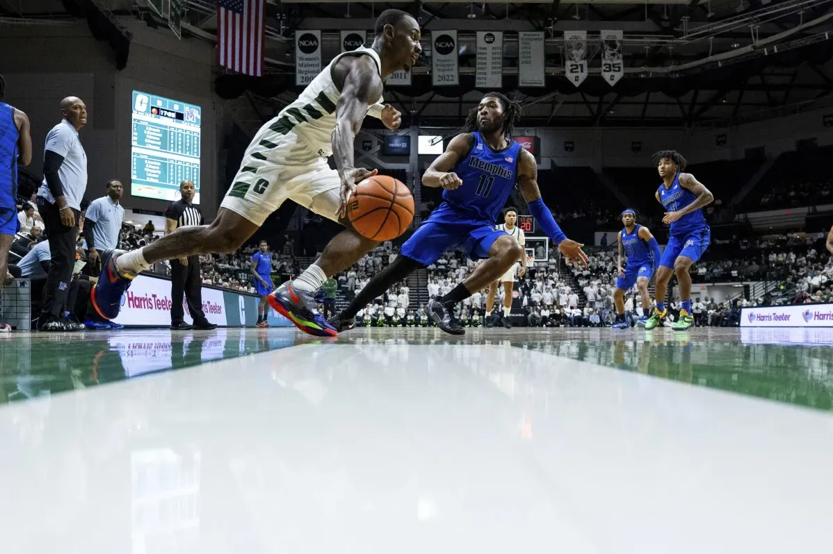 لاعب كرة سلة يت dribble الكرة تحت الضغط في مباراة بين ممفيس وتشارلوت، بينما يظهر لاعب آخر ينافسه، وسط جمهور في الخلفية.