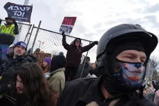 محتجون في مينيابوليس يحملون لافتات تعبر عن الغضب ضد سياسة الهجرة، مع وجود عناصر من الشرطة في الخلفية.