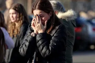 امرأة شابة تبكي وتغطي وجهها بيديها، محاطة بمجموعة من الأشخاص في موقع حادث إطلاق نار خلال مباراة هوكي للشباب في رود آيلاند.