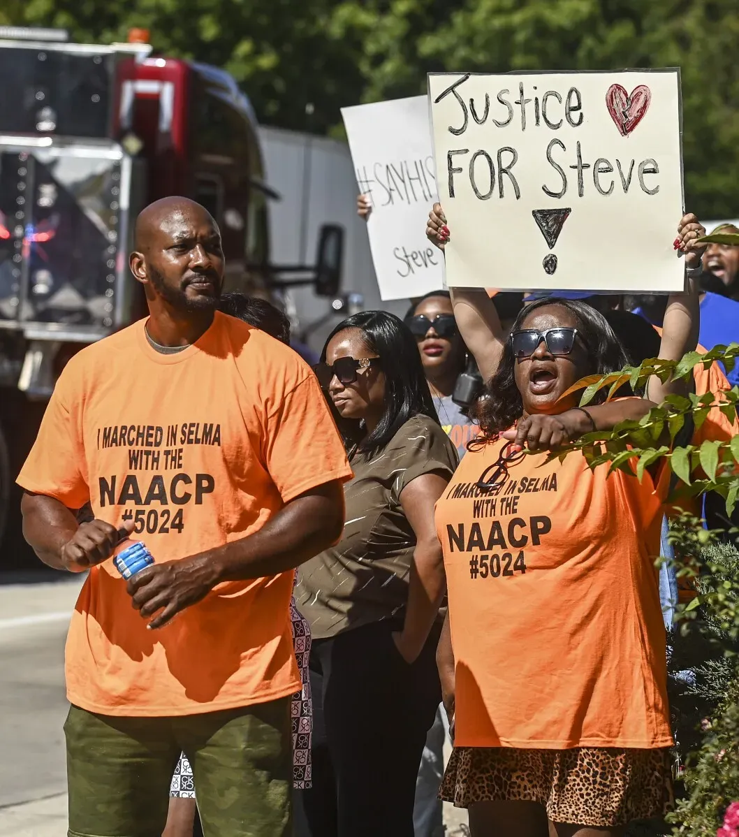 متظاهرون يحملون لافتات لطلب العدالة لستيف بيركنز، مرتدين قمصان برتقالية تحمل شعار NAACP، في تجمع احتجاجي بألاباما.