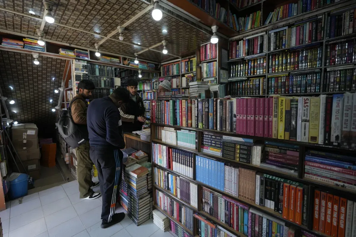 مكتبة في سريناغار تُظهر عددًا كبيرًا من الكتب، حيث يقوم ثلاثة أشخاص بالتفاعل مع البائع، في ظل مداهمات الشرطة لمصادرة مؤلفات محظورة.