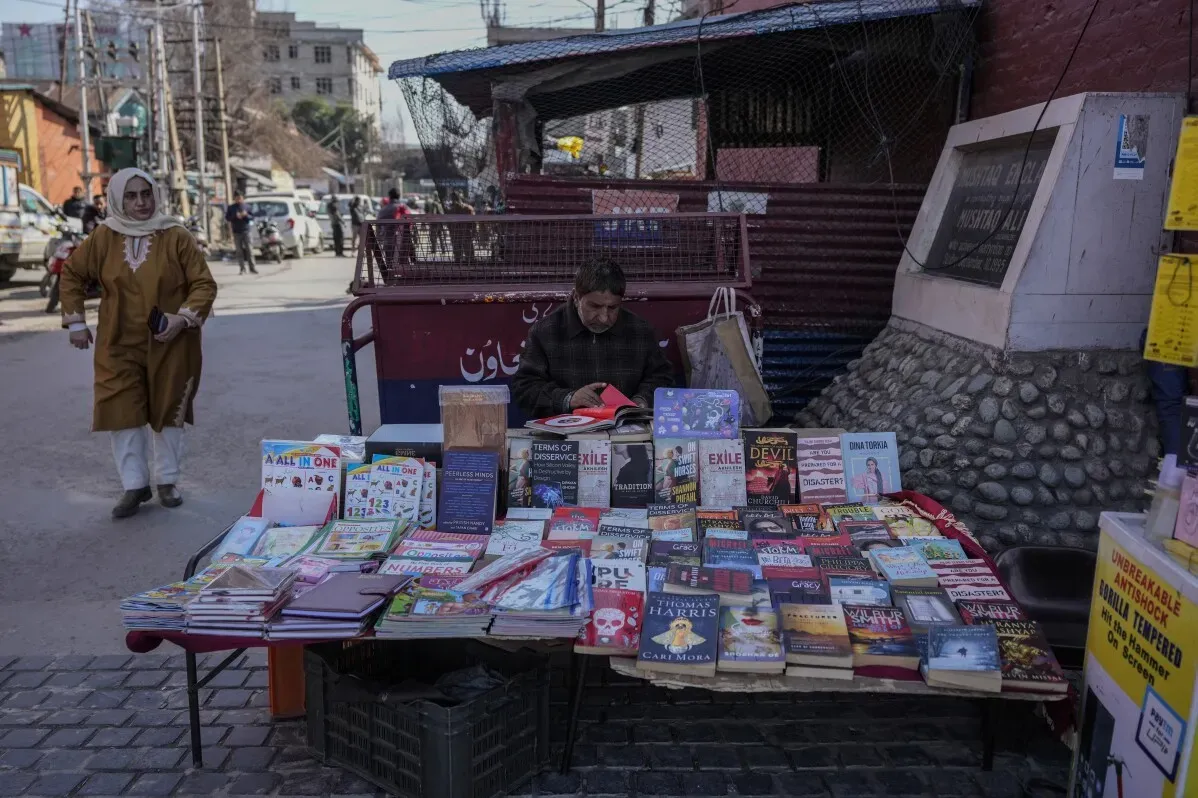 بائع كتب يجلس أمام طاولة مليئة بالكتب في سريناغار، بينما تمر امرأة في الخلفية، في ظل مداهمات الشرطة لمصادرة الكتب المحظورة.