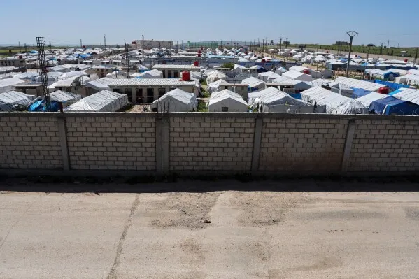 مخيم للاجئين في شمال سوريا، يظهر فيه tents بيضاء وزرقاء، يرمز إلى الظروف الصعبة التي تواجه النساء والأطفال العائدين إلى أستراليا.