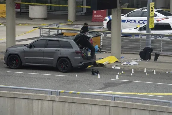 حادث إطلاق نار خارج مطار بيرسون في تورونتو، مع وجود سيارة سوداء وصناديق تحقيق، ووجود كثيف للشرطة في المنطقة.