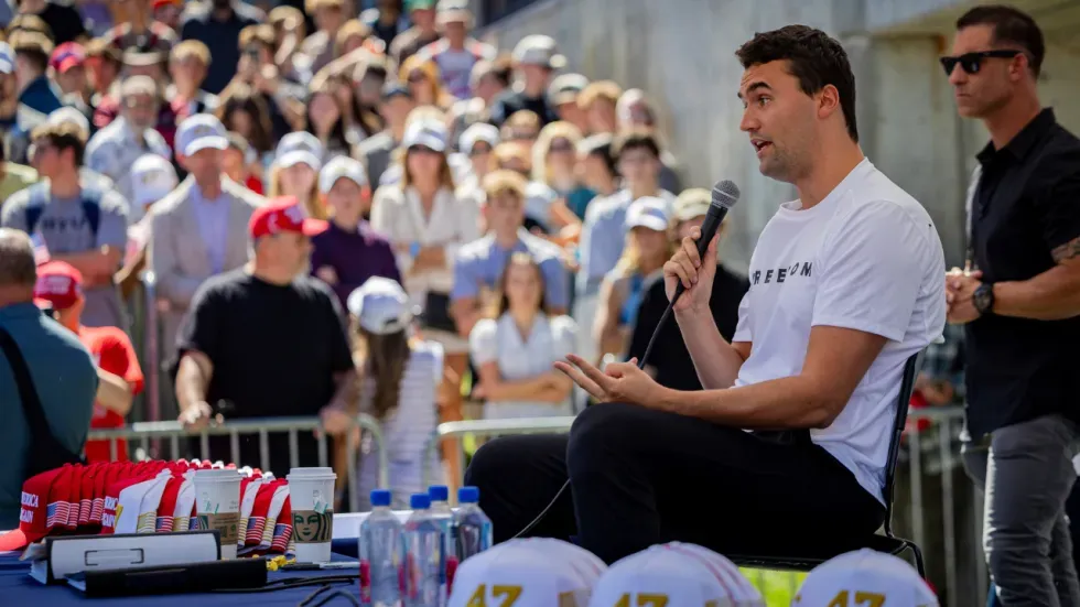 تشارلي كيرك يتحدث في فعالية جماهيرية بولاية يوتا، بينما يستمع إليه حشد كبير من الشباب، مع وجود عناصر أمنية في الخلفية.